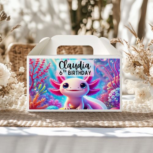 Gift box with axolotl design and 'Claudia 6th Birthday' text, placed on a woven surface with flowers.